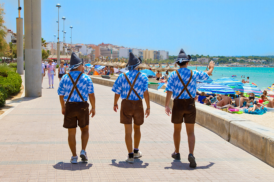 Drei Männer in Lederhosen läufen an der Strandpromenade auf Mallorca